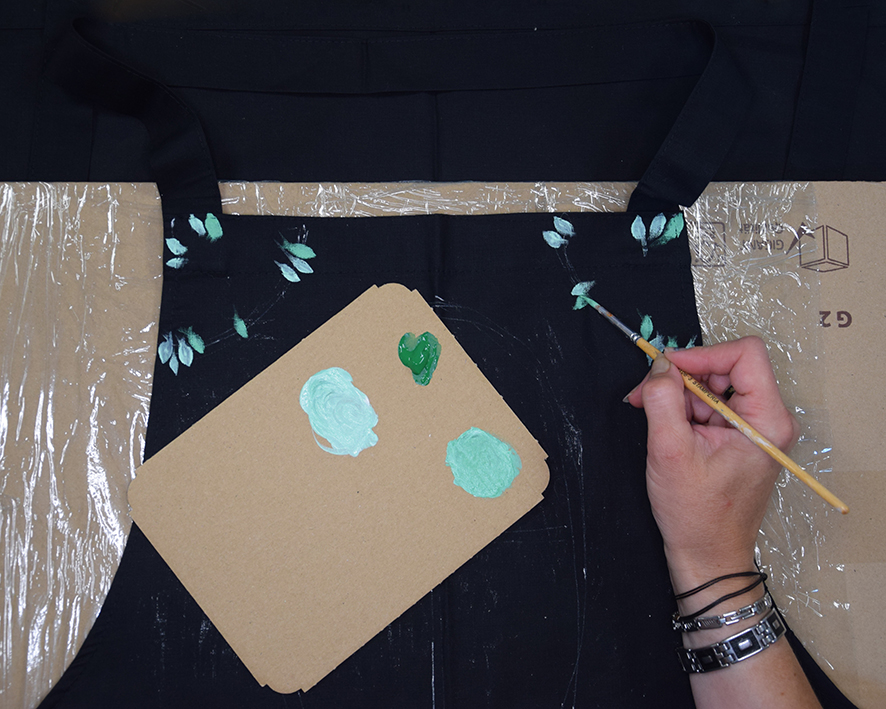 Žena pomocí lednějších odstínů zelené barvy na textil maluje listy od nejblednějších po nejtmavší.