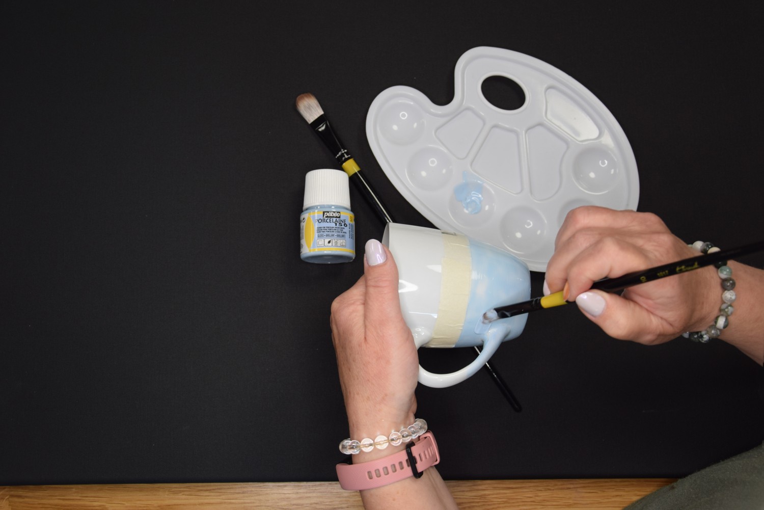 Žena používá bledomodrou barvu na porcelán a natírá s ní spodní stranu hrnku.