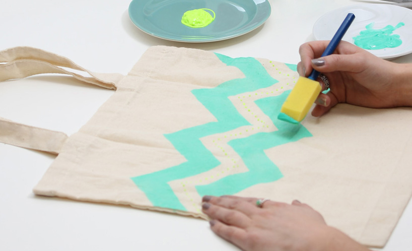 Dítě maluje na textil pomocí tyrkysové barvy a tupovacího štětce.