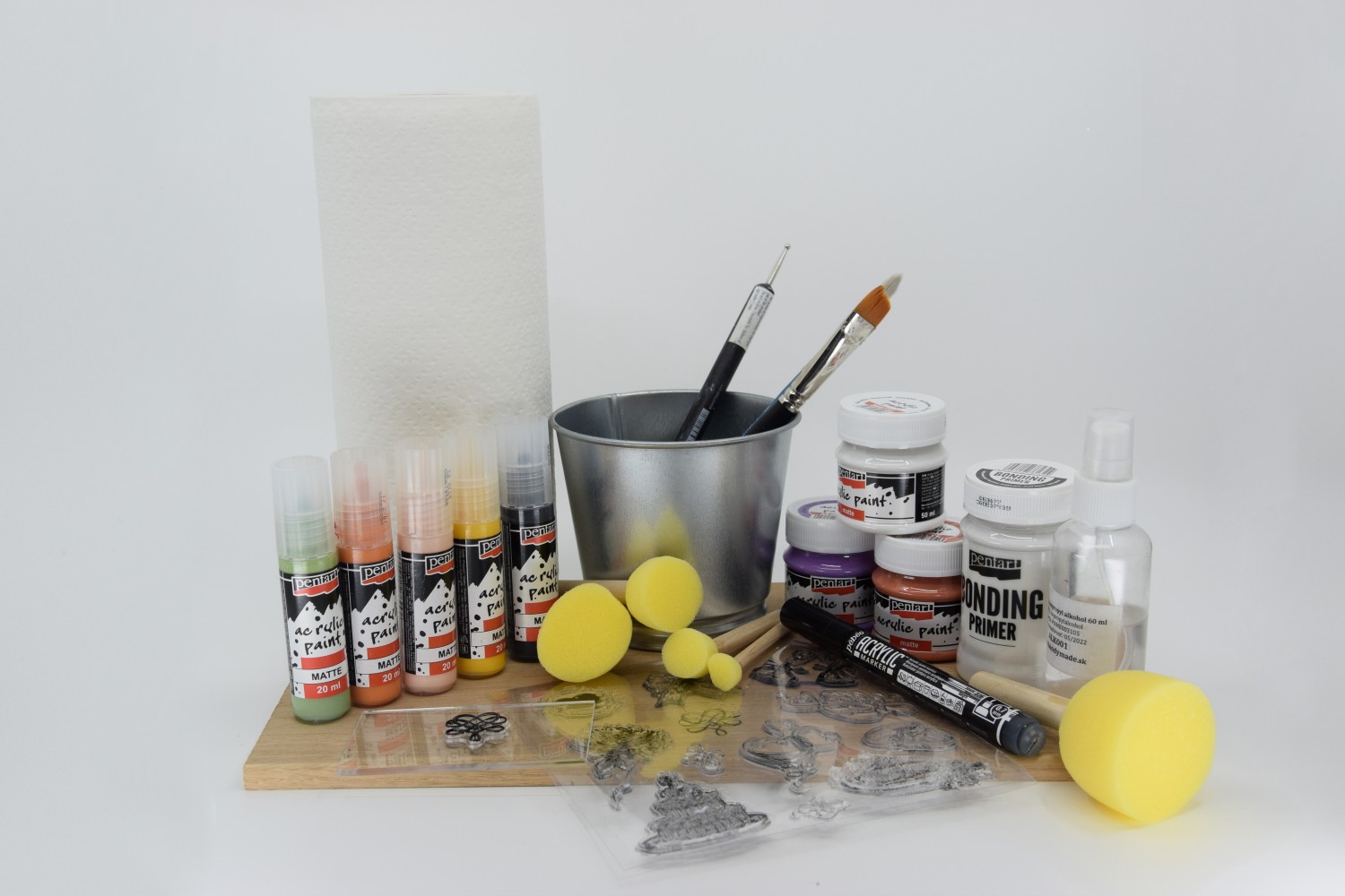 Všechny potřebné produkty na malování květináče jsou položeny na desce a za ní je bílé pozadí. Jsou tu štětce, razítka, tužka, Acrylic marker, akrylové barvy Acrylic paint, utěrky a čistý kovový květináč.